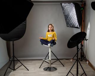 Photographing children in professional photo studio with lighting equipment. Child girl is posing for professional photos with modern flashes in amateur home studio on grey background