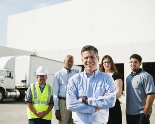 Man standing in front of a warehouse with workers in the background. 