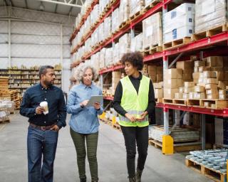 Three workers are in a warehouse discussing business. 