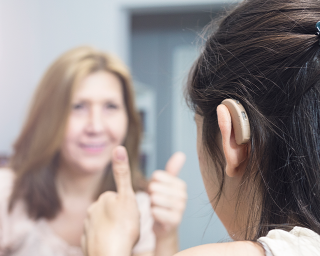 A person with a hearing aid gives a thumbs-up