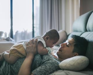 Cozy moment Asian Chinese father lying on bed playing with baby boy weekend morning 