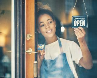 Shot of a young woman hanging an open sign on the window of a cafe