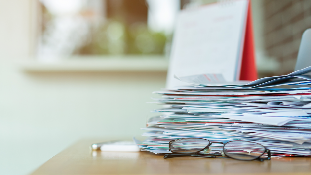 A stack of papers on a desk behind a pair of glasses